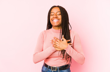 Young african american woman isolated on a pink background laughing keeping hands on heart, concept of happiness.