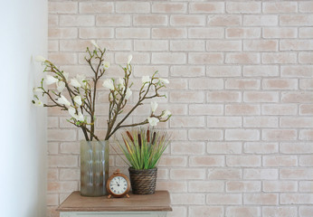 Artificial flower and green grass in vase with clock on the table in modern living room. Interior...