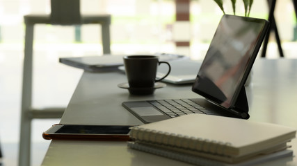 Side view of workspace with digital tablet, notebooks, smartphone and supplies on white table