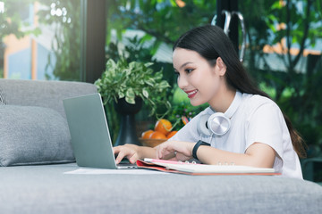 Beautiful asian woman smiling and looking at laptop in living room. Working, Learning from home concept.