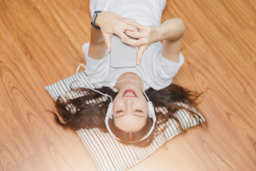 Obraz na płótnie Canvas Top view of young beautiful asian woman with headphone and listening music from smartphone while lying on the floor at home.