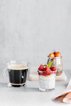 Glass cup of coffee with chia pudding garnished with raspberries and white cherries with wheat crispbreads with nut spread and jam with almond pieces