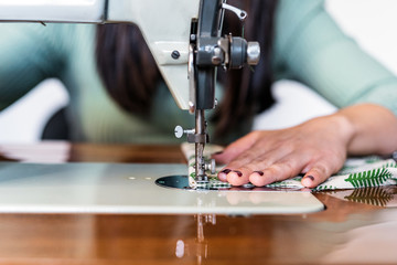 Unrecognizable craftswoman using modern sewing machine while creating soft fabric samples with creative green pattern near lamp in loft style workshop