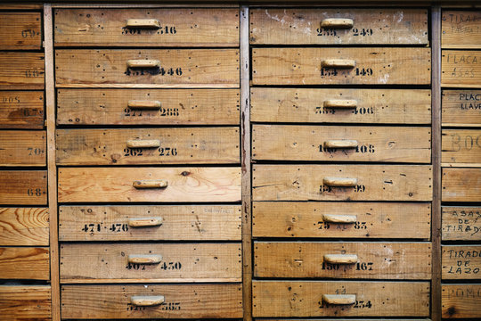 Archive representing identical light brown wooden drawers with rectangular handles and numbers on uneven surface with spots and words in workshop