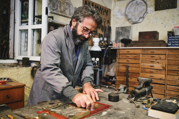 Craftsman cleaning etching with creative ornament in golden frame using hard piece of fabric in workshop