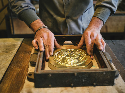 Crop unrecognizable goldsmith placing metal pattern into molding box during casting process while working in workshop