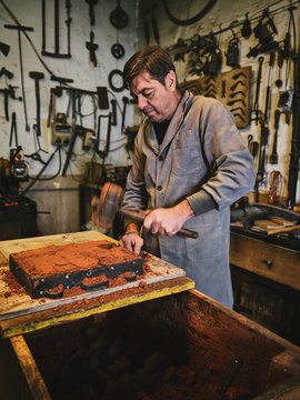 Side view of skilled male master with professional tool packing sand in molding box during sand casting process in goldsmith workshop