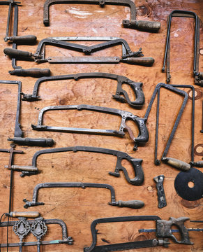 Top view of various aged metal hacksaws for craft work arranged on weathered wooden surface in workshop