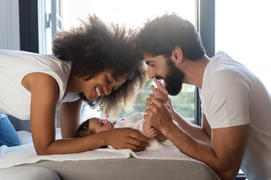 Side view of delighted multiethnic family playing with cute baby on sofa at home