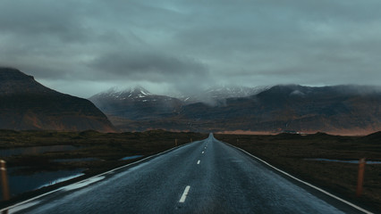 Majestic view of narrow empty straight asphalt roadway surrounded by mountains under sky with low clouds in daylight in Iceland