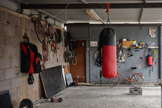 Interior of shabby country garage gym with boxing bag bicycles and sports equipment placed on concrete floor near old fashioned boombox
