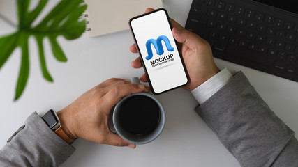 Male entrepreneur take a break with coffee and mock up smartphone on office desk