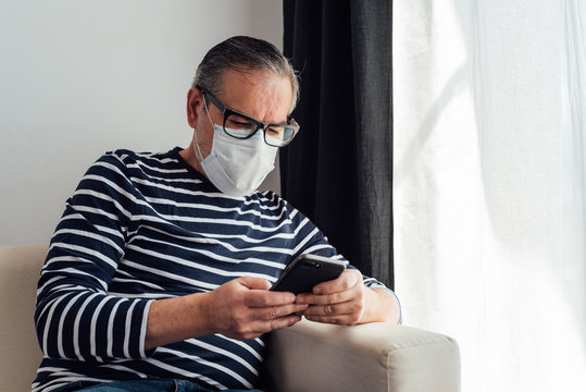 Focused male in glasses using on mobile phone and laptop while working at home because of quarantine