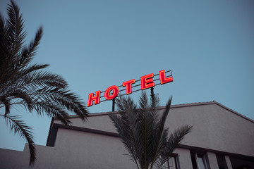 Low angle of illuminated hotel word made with big red neon letters and placed on modern building roof in dusk