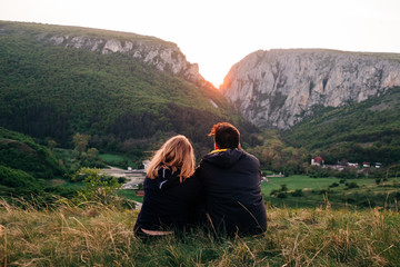 Back view of unrecognizable couple of tourists standing on background of mountain range and tenderly embracing while enjoying holiday in Transylvania