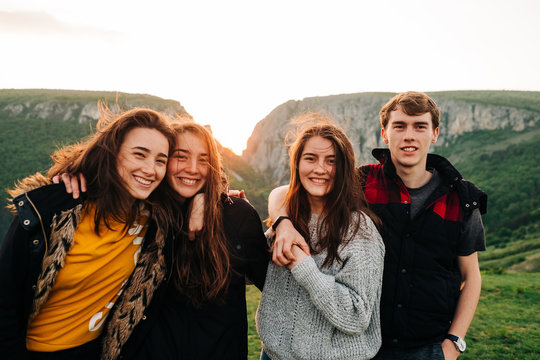 Group of happy friends hugging together on background of spectacular mountainous landscape in Transylvania and cheerfully looking at camera during vacation