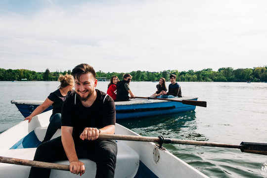 Positive laughing young friends chilling on boats and browsing mobile phone while spending weekend together on peaceful tranquil pond in Saint George, Transylvania, Romania