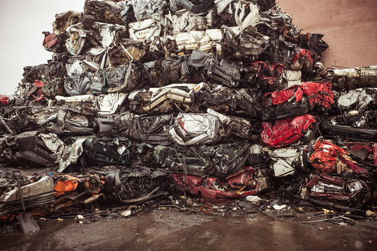 Dump of heap of ruined dirty multicolored autos after accident put on wet pavement near concrete wall