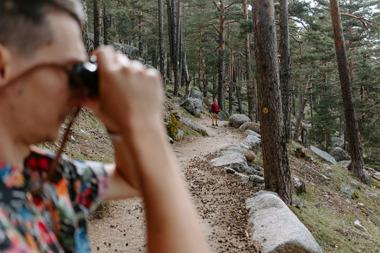 Side view of male tourist in colorful shirt standing on slope of mountain covered with coniferous forest and observing environment with binoculars during hiking in Navacerrada in Spain