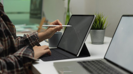 Female university student using digital tablet with stylus pen on worktable with mock up laptop