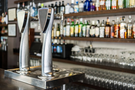 Metallic beer column placed on bar counter against shelves with alcoholic drinks in glass bottles