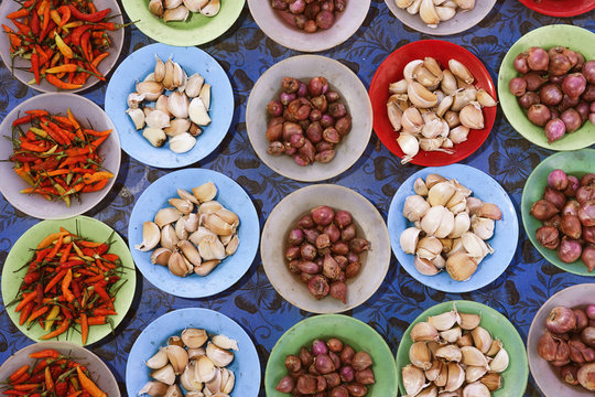 Top view of garlic and onions in bowls placed on counter with dried chili peppers in local bazaar