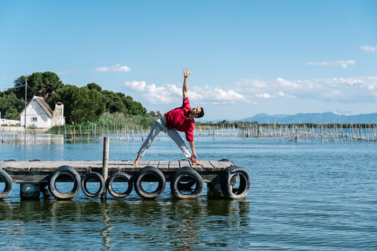 Full body of peaceful barefooted guy in casual wear performing Lord of the Dance yoga pose and and Gyan mudra on lumber pier on sunny day