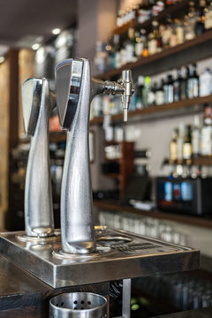 Metallic beer column placed on bar counter against shelves with alcoholic drinks in glass bottles