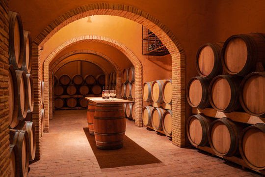 Interior of contemporary spacious winery storage with wooden barrels and cozy table in center for wine tasting