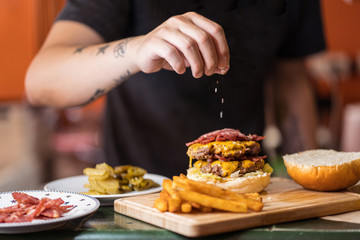 Unrecognizable male chef adding salt to burger while standing at table in cafe