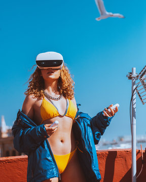 Sensual unrecognizable female traveler in swimwear and VR googles entertaining while watching video with open mouth on roof under blue sky in sunlight