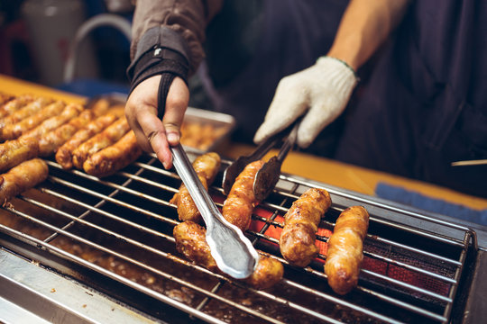 Faceless chef standing at counter in Night Market in Taiwan and cooking palatable chicken sausages on grill