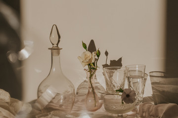 High angle of white delicate flowers in small vase placed on table covered with tulle and arranged with vintage styled glasses and decanter