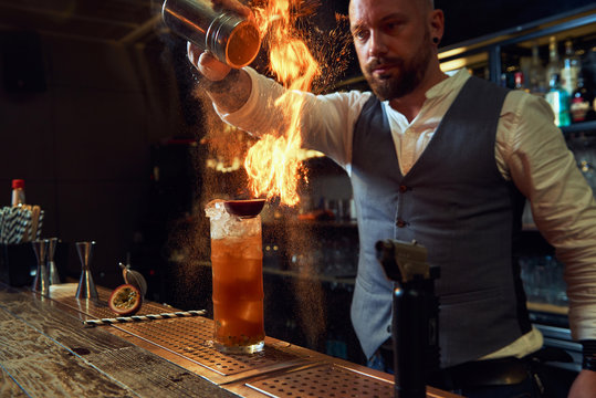 Professional young bartender burning a cocktail with salt and fire with glass in flame in the bar