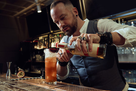 Professional young bartender holding bottle while preparing a cocktail in the bar
