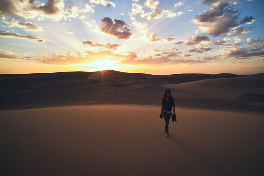 From above of anonymous female tourist strolling in sandy terrain in desert with dry wavy surface under cloudy sky at bright sundown