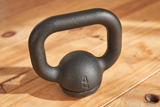 From above of cast iron four kilogram kettlebell on wooden floor in light of sun