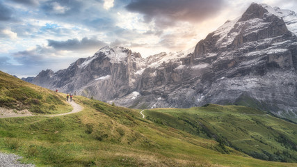 From above back view of anonymous traveler strolling on rough narrow walkway surrounded by magnificent green ridge under cloudy sky during trip in daylight