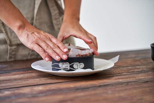 Crop view of anonymous female in apron removing cake from baking form while preparing dessert in kitchen