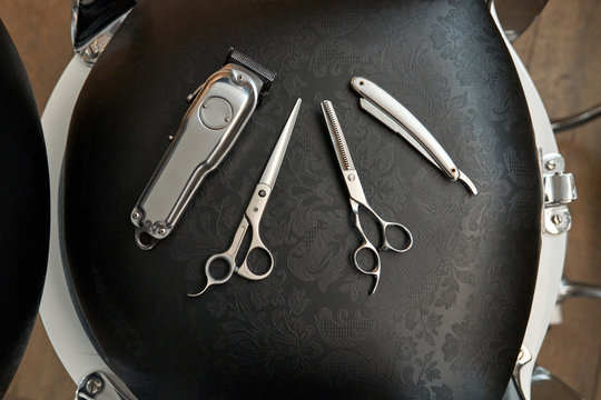 Top view of set of various hairdressing instruments including scissors trimmer and razor placed on chair in barbershop