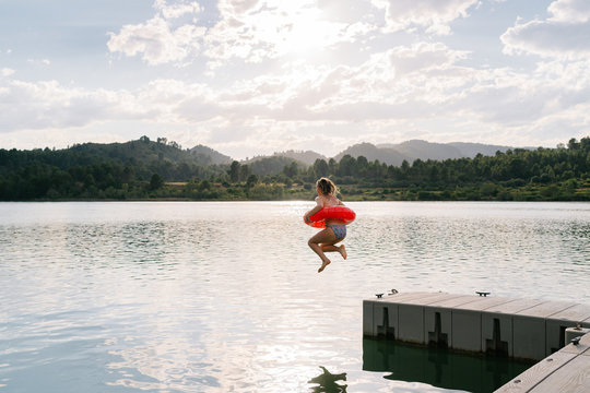Side view of teenage girl in bikini and rubber ring in moment of jumping in water of pond in summer