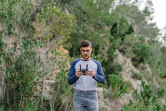 Focused male with remote controller operating unmanned drone and recording video of spectacular landscape