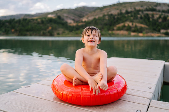 Adorable preteen child with wet hair relaxing on inflatable ring on wooden pier during summer vacation near lake