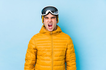 Young skier man wearing snowboard goggles isolated screaming very angry and aggressive.