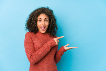 Young african american curly hair woman excited holding a copy space on palm.