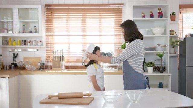 Mother wearing chef hat for child before start make bakery in kichen room. Mom and little japanese girl feeling happy, cheerful and enjoy in weekend. Contemporary free time with children concept