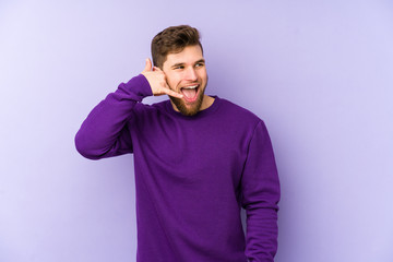 Young caucasian man isolated on purple background showing a mobile phone call gesture with fingers.