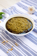 Homemade Basil Pesto with Parmesan and Pine Nuts on a white wooden background, low angle view.