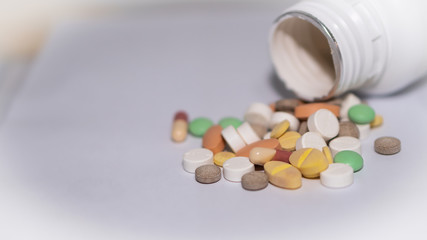 Many pills are poured on white paper and bottle in the background.