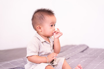 Adorable asian baby boy sucking thumb while sitting in bedroom,Happy new born kid .
